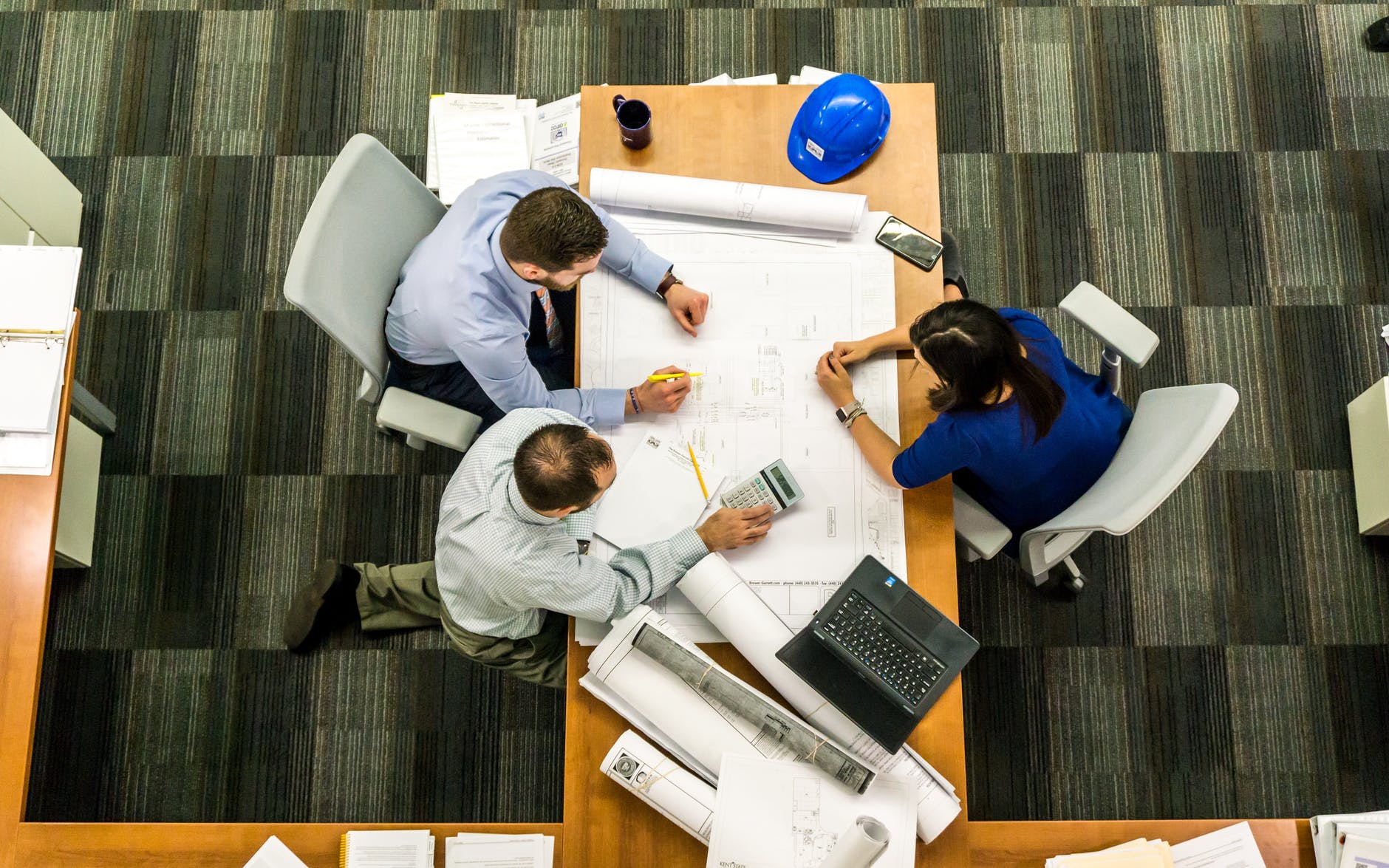 Three people sitting around a table reviewing drawings